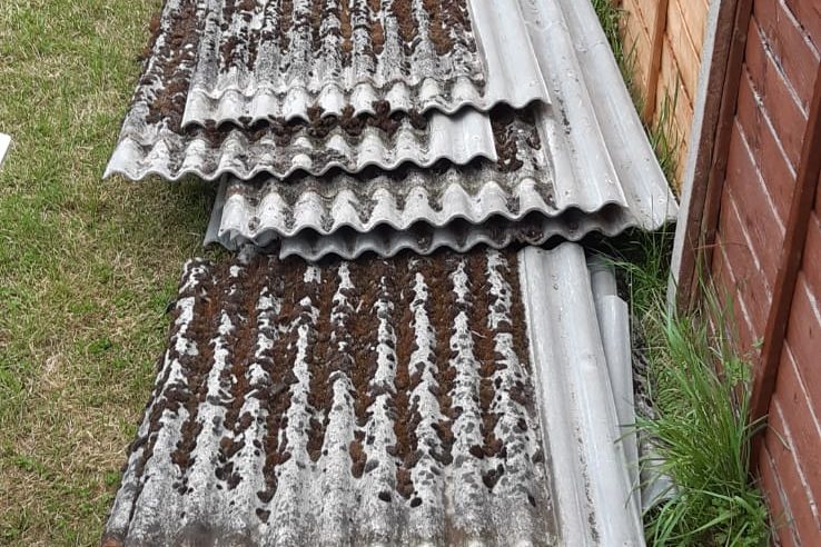 A pile of corrugated roofing sheets with soil debris on top